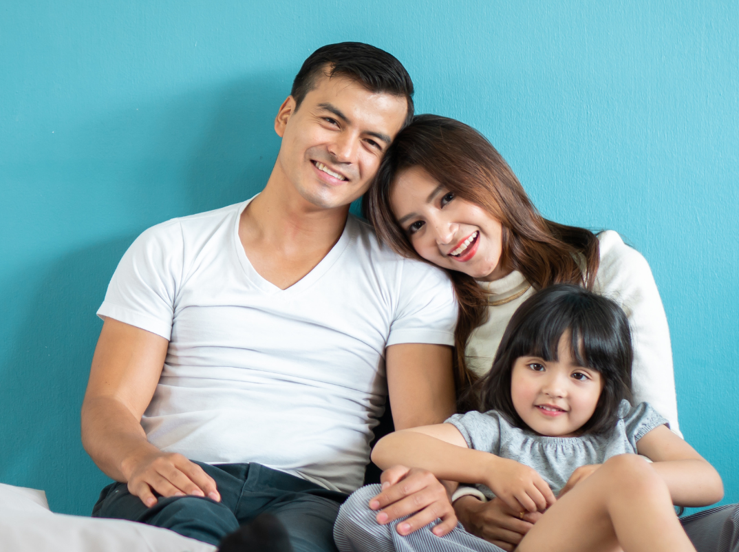 A family of three smiling on a couch.